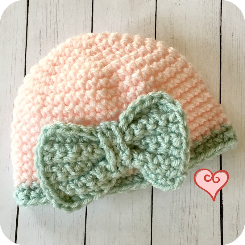 Peut inclure: Un bonnet en crochet rose avec un n&oelig;ud en crochet vert. Le bonnet est r&eacute;alis&eacute; avec des points de crochet simples et le n&oelig;ud avec des points de crochet doubles.