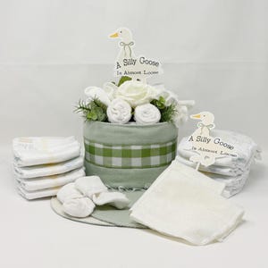 May include: A baby gift set featuring a green and white gingham-patterned container with a floral arrangement and the text "A Silly Goose Is Almost Loose." The set includes diapers, washcloths, and baby socks.