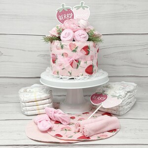 May include: A pink and red diaper cake decorated with strawberries and flowers. The cake is topped with a sign that says "Berry Sweet".
