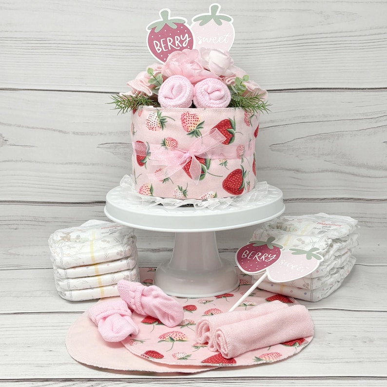 May include: A pink and red diaper cake decorated with strawberries and flowers. The cake is topped with a sign that says "Berry Sweet".