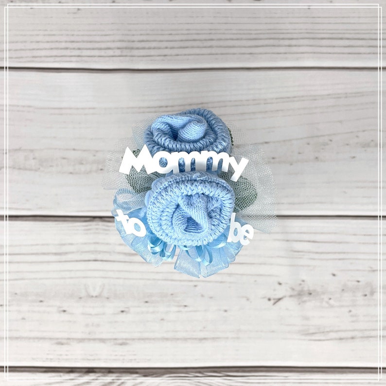 May include: A blue sock flower bouquet with white tulle and a white banner that says "Mommy to be".