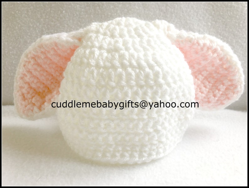 Peut inclure: Chapeau de b&eacute;b&eacute; en crochet blanc avec des oreilles en crochet rose. Le chapeau a un motif de point textur&eacute;. Le texte "cuddlemebabygifts@yahoo.com" est visible sur le chapeau.