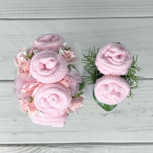 May include: A bouquet of pink baby socks arranged to look like roses, with pink and white flowers and green leaves. The bouquet is tied with a pink ribbon and white tulle.