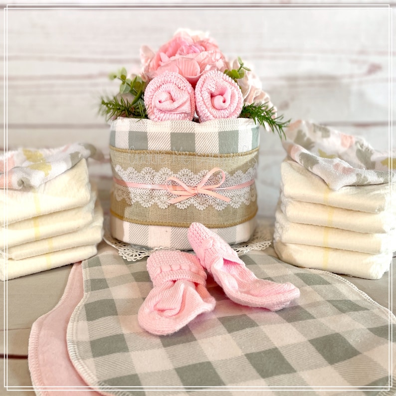 May include: A baby shower gift basket with a pink and gray gingham pattern. The basket is filled with pink and white baby socks, a pink and white diaper cake, and a pink and white burp cloth.