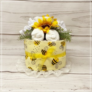 Puede incluir: Un pastel de pañales con temática de abejas amarillas y negras con un girasol y toallitas blancas para bebés. El pastel está decorado con una cinta amarilla.