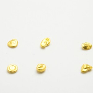 May include: Seven small, irregularly shaped pieces of gold leaf on a white background.