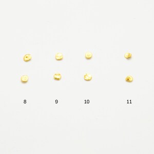 May include: Twelve small, round, gold-colored metal pieces arranged in two rows of six. The pieces are numbered 7 through 12.