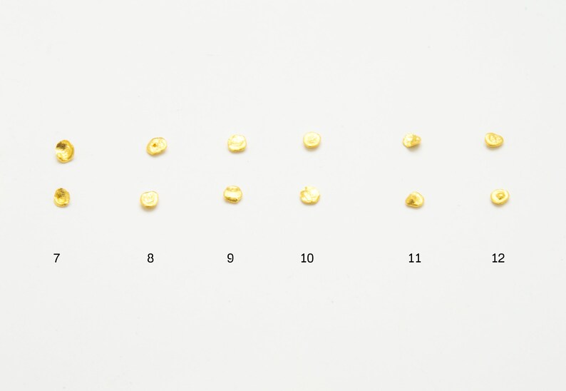 May include: Twelve small, round, gold-colored metal pieces arranged in two rows of six. The pieces are numbered 7 through 12.