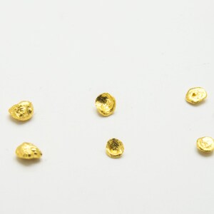 May include: A collection of small, gold-colored, irregularly shaped metal pieces scattered on a white surface.