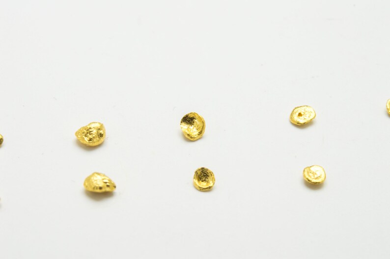 May include: A collection of small, gold-colored, irregularly shaped metal pieces scattered on a white surface.
