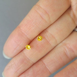 May include: A pair of small, gold-colored stud earrings. The earrings are round and have a slightly textured surface.
