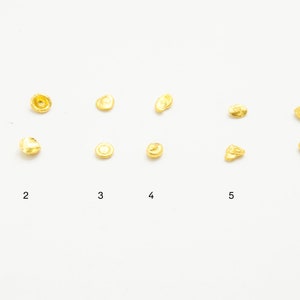 May include: Six rows of gold nuggets of varying sizes and shapes. The nuggets are arranged in rows, with the largest nuggets at the top and the smallest nuggets at the bottom.