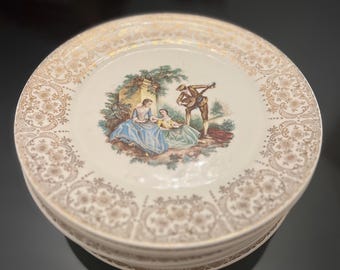 Może przedstawiać: Zestaw czterech białych ceramicznych talerzy z pozłacanym rantem i wzorem kwiatowym. Środek każdego talerza zdobi kolorowa ilustracja pary w ogrodzie.