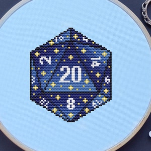 May include: A blue and gold 20-sided die with a starry night design, stitched on a light blue fabric in a wooden embroidery hoop.