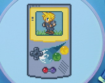 May include: A cross-stitch embroidery hoop with a pixelated image of a handheld video game console. The game screen shows a character from a popular video game. The hoop is on a blue background with embroidery floss and scissors.