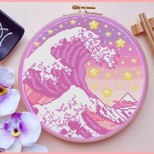 Może przedstawiać: Haft krzyżykowy w kolorze różowym i żółtym przedstawiający Wielką Falę u wybrzeży Kanagawy, słynny japoński drzeworyt autorstwa Hokusai, w okrągłym drewnianym obręczy do haftu.