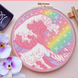 May include: A pink and white cross-stitch embroidery of a wave with a rainbow design. The embroidery is framed in a wooden hoop.