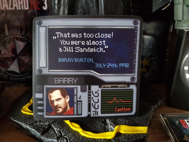 K&ouml;nnte beinhalten: Ein schwarzer und grauer Videospiel-Aufkleber mit einem pixeligen Bild eines Mannes mit einem roten Hemd vor einem schwarzen Hintergrund. Der Text auf dem Aufkleber lautet "That was too close! You were almost a Jill Sandwich." Barry Burton, July 24th 1998. Der Aufkleber zeigt auch ein pixeliges Bild eines Herzfrequenzmonitors mit dem Wort "Caution" darunter.