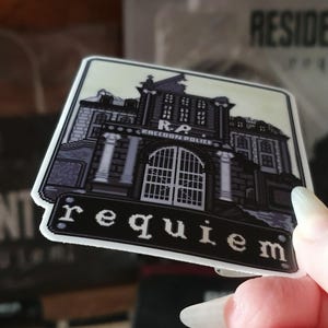 May include: A square sticker featuring a pixelated illustration of a building with the text "R.P. RACCOON POLICE" above the entrance and the word "requiem" below. The sticker has a white border and a light beige background.