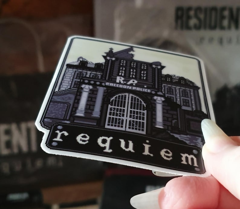 May include: A square sticker featuring a pixelated illustration of a building with the text "R.P. RACCOON POLICE" above the entrance and the word "requiem" below. The sticker has a white border and a light beige background.