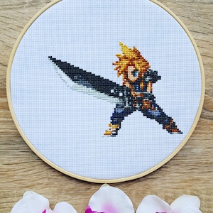 May include: Cross-stitch embroidery of a video game character holding a sword. The character is depicted in a pixelated style, with a yellow and blonde hair, a black and blue outfit, and a large sword with a silver blade.