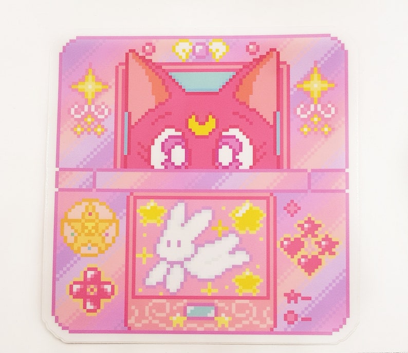 May include: A pink and purple pixel art design of a handheld video game console with a pink cat character on the screen. The game features a white bunny character with wings and stars.