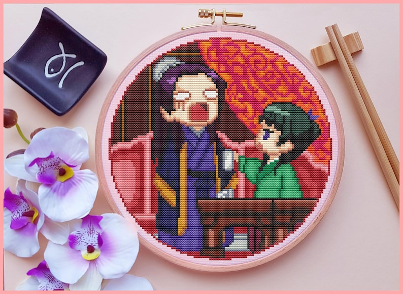 May include: Cross-stitch embroidery in a wooden hoop featuring two cartoon figures in a scene with a table. The figures are in purple and green clothing. A small black dish with a white symbol and chopsticks are also in the image.
