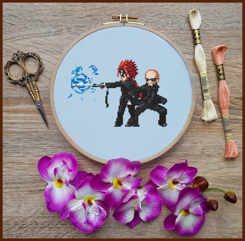 May include: A cross-stitch embroidery featuring two pixelated figures in black outfits, one with red hair, wielding a blue energy blast. The embroidery is set in a wooden hoop, with scissors, thread, and purple orchids.