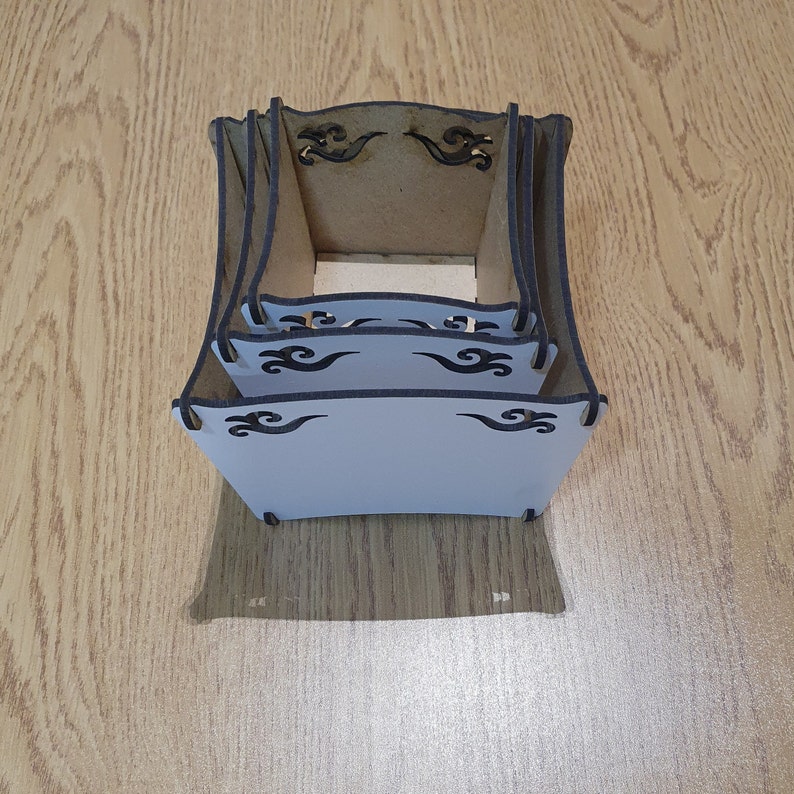 May include: A set of three wooden boxes with intricate black wave designs. The boxes are stacked on top of each other and are made of a light brown wood.
