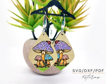 May include: A pair of wooden earrings with a whimsical mushroom design. The earrings feature a purple mushroom with white spots, a pink mushroom, and a blue mushroom. Each mushroom has a ladybug on top. The earrings are hanging from silver hooks.