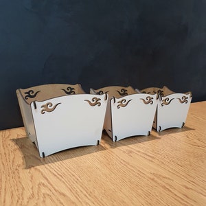 May include: Three white wooden boxes with decorative cutouts. The boxes are nested inside each other, with the largest box in the front and the smallest box in the back.