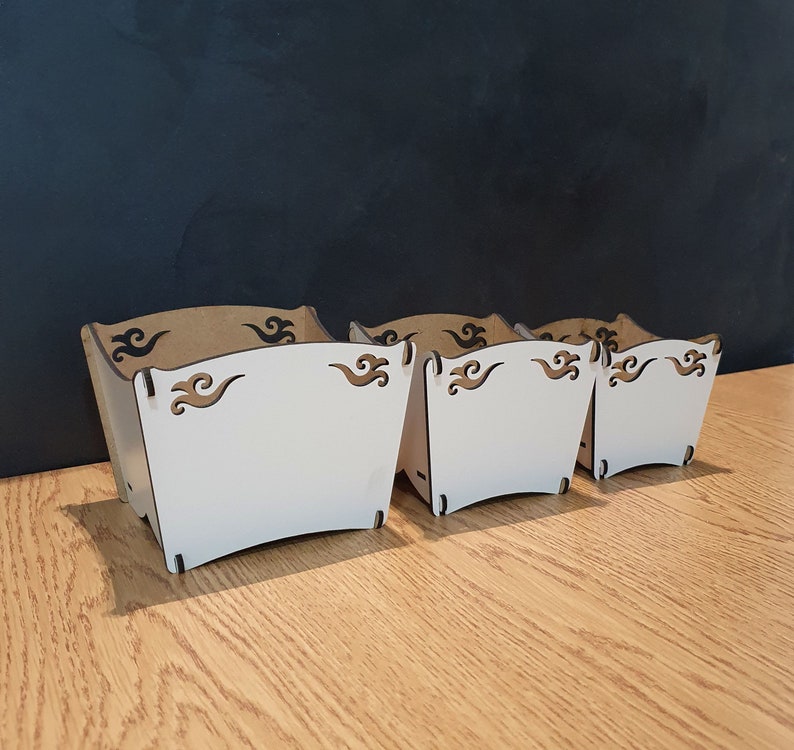 May include: Three white wooden boxes with decorative cutouts. The boxes are nested inside each other, with the largest box in the front and the smallest box in the back.