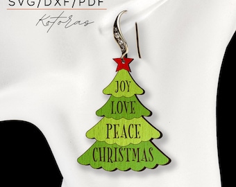 May include: Green Christmas tree-shaped earrings with the words "Joy", "Love", "Peace", and "Christmas" on each earring. The earrings are made of wood and have a silver hook.