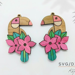 Op de afbeelding: Een paar houten toekan oorbellen met roze, groene en bruine accenten. Elke oorbel heeft een toekanvorm met een roze snavel en een bloemenontwerp met roze bloemen en groene bladeren. Voor SVG-, DXF-- en PDF-formaten.
