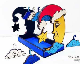 May include: A wooden earring holder shaped like a crescent moon with a star and clouds. The moon is painted yellow with a smiling face and a red Santa hat. The other moon is black with a star and clouds. The holder has a blue tray for storing earrings.