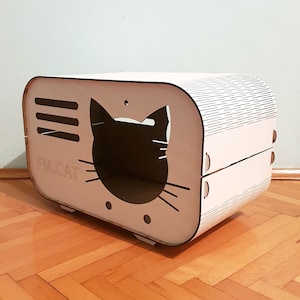Pode incluir: Cama de gato de madeira branca em forma de rádio vintage com um recorte de silhueta de gato preto. A cama tem o texto "FM.CAT" na frente.
