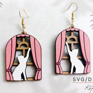 May include: A pair of pink and white wooden earrings featuring a cat silhouette reaching out of a window with curtains. The earrings are labeled "SVG/DXF/PDF KotoRas".
