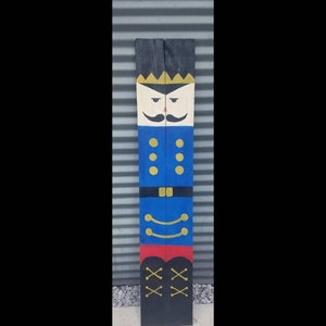 May include: A wooden nutcracker painted in blue, red, yellow, and black. The nutcracker has a gold crown, a mustache, and a black hat.