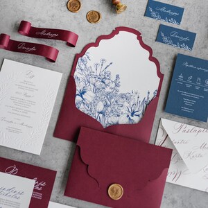 Könnte beinhalten: Ein Satz Hochzeitseinladungen mit einem burgunderfarbenen Umschlag, einem weißen Innenumschlag und einer weißen Einladungskarte mit einem blauen Blumendesign. Die Einladungskarte enthält den Text "Du" und "Mindaugas & Diningda" in kursiver Schrift. Der Umschlag ist mit einem Wachssiegel mit einem goldenen Design versehen.