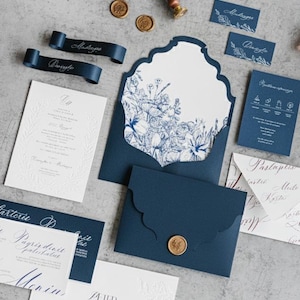 Könnte beinhalten: Eine Auswahl an marineblauen und weißen Hochzeitsbriefpapier. Enthält Einladungen, Umschläge, Tischkarten und Bänder. Blumendesign auf der Innenseite des Umschlags. Goldene Wachssiegel und ein Schlüsselanhänger sind ebenfalls vorhanden.