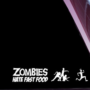Könnte beinhalten: Ein weißer Vinyl-Aufkleber mit dem Text "Zombies Hate Fast Food" und drei weißen Silhouetten von Zombies, die rennen. Der Aufkleber befindet sich auf einem dunkelroten Auto.