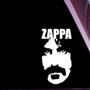 Puede incluir: Una pegatina de vinilo blanco con una silueta en blanco y negro de la cara de Frank Zappa y la palabra "Zappa" en letras blancas.