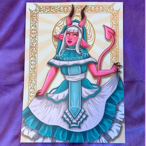 Peut inclure: Illustration d'une figure rose semblable à un démon, vêtue d'une robe turquoise et blanche avec une longue queue rose. La figure a des cornes, un halo et le texte "CCDOCD" sur la robe. L'œuvre est encadrée d'une bordure dorée.