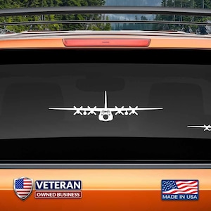 May include: White vinyl decal of a C-130 Hercules aircraft silhouette on a black car window. The decal is made in the USA and is a veteran owned business. The text "www.fegraphics.com Flight Engineered Graphics Aircraft Decals" is at the bottom of the image.