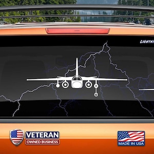 May include: A white vinyl decal of a C-130 Hercules aircraft with a lightning bolt design. The decal is on the back window of a car. The text "LIGHTNING NOT INCLUDED" is on the decal. The text "VETERAN OWNED BUSINESS" is on the car. The text "MADE IN USA" is on the car. The text "www.fegraphics.com Flight Engineered Graphics Aircraft Decals" is on the bottom of the image. The text "VETERAN OWNED BUSINESS" is on the bottom of the image.
