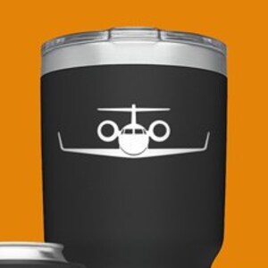 May include: Four Yeti tumblers with a plane silhouette design. The tumblers are in black, blue, green, and silver. The tumblers are all different sizes. The largest tumbler is black with a white plane silhouette. The smallest tumbler is silver with a black plane silhouette. The blue tumbler is a can cooler with a white plane silhouette. The green tumbler is a standard size with a black plane silhouette.
