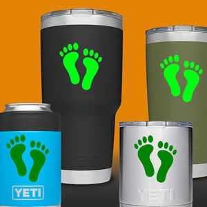 May include: Three different sizes of YETI tumblers with a green footprint design. The tumblers are black, blue, and silver.