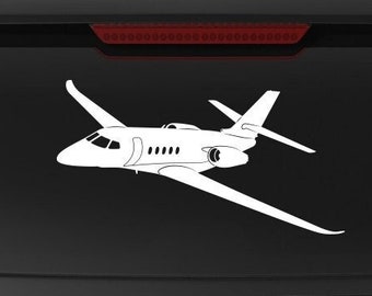 May include: White vinyl decal of two private jets in flight, applied to the rear window of a black SUV. The decal is a simple outline, showing the shape of the aircraft. The SUV also has a Veteran Owned Business emblem.