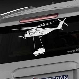 May include: A white decal of a helicopter carrying a tank, affixed to the rear window of a silver SUV. The decal includes the text "www.fegraphics.com" and a "Veteran Owned Business" emblem.