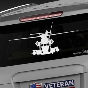 May include: A gray SUV with a white silhouette of a helicopter on the back window. The vehicle has a sticker that says "Veteran Owned Business" and the website "www.fegraphics.com" is printed on the back bumper.